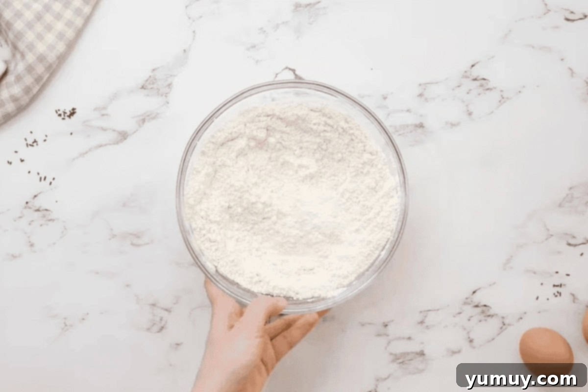 A glass bowl containing white flour, ready to be combined with other dry ingredients.