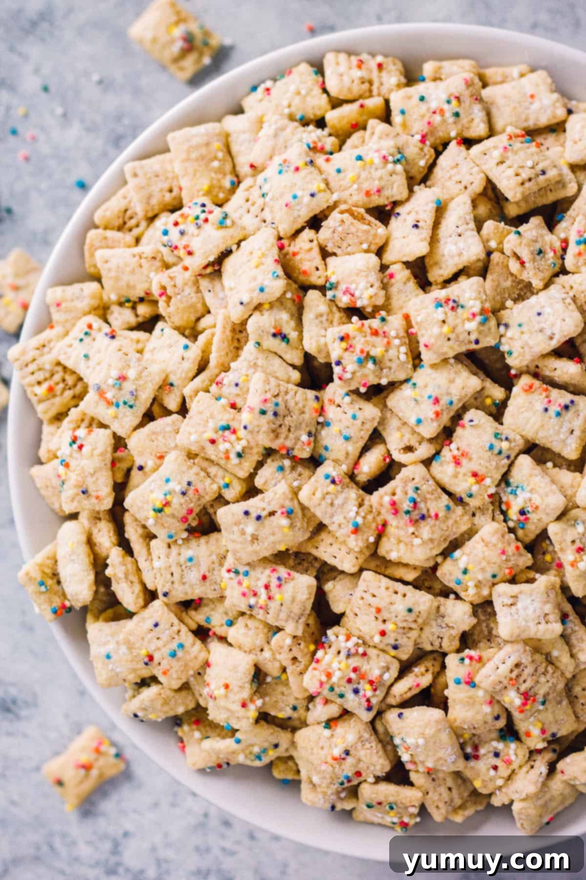 A beautiful white bowl brimming with homemade birthday cake puppy chow, generously coated with white chocolate and rainbow sprinkles.