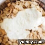 Pouring melted white chocolate over Rice Chex cereal in a mixing bowl.