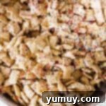 Stirring colorful rainbow sprinkles into the chocolate-coated Chex cereal mixture.