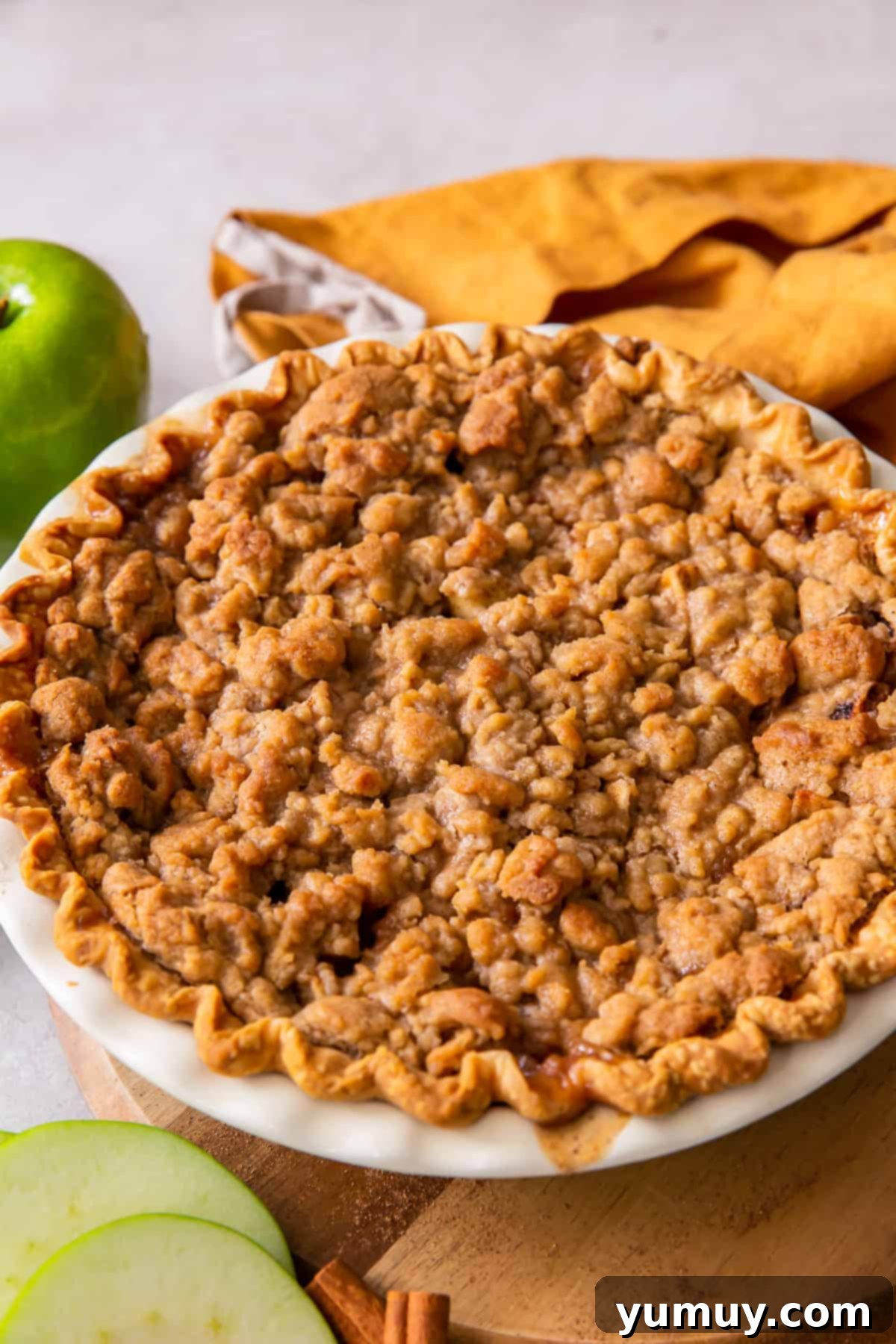 Homestyle Dutch Apple Pie 3 A perfectly baked whole Dutch apple pie, topped with a golden streusel crumble, resting in a white pie dish.
