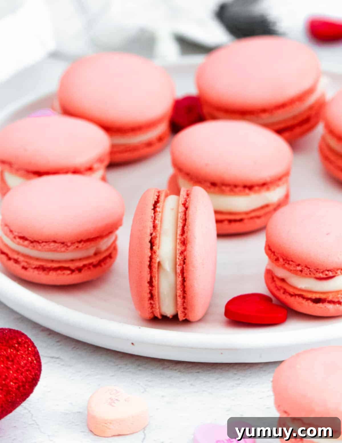 Exquisite pink Valentine's Day macarons with cream cheese filling, artfully arranged on a pristine white plate, promising a delightful dessert experience.