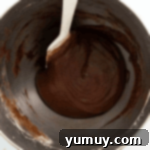 chilled chocolate madeleine batter in a stainless mixing bowl with a rubber spatula.