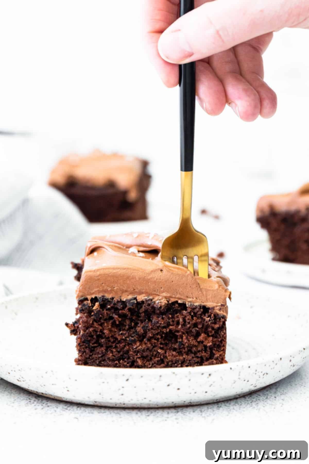 Fork dipping into a slice of chocolate cake with chocolate frosting.