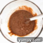 chocolate cake batter in a glass bowl with a whisk.