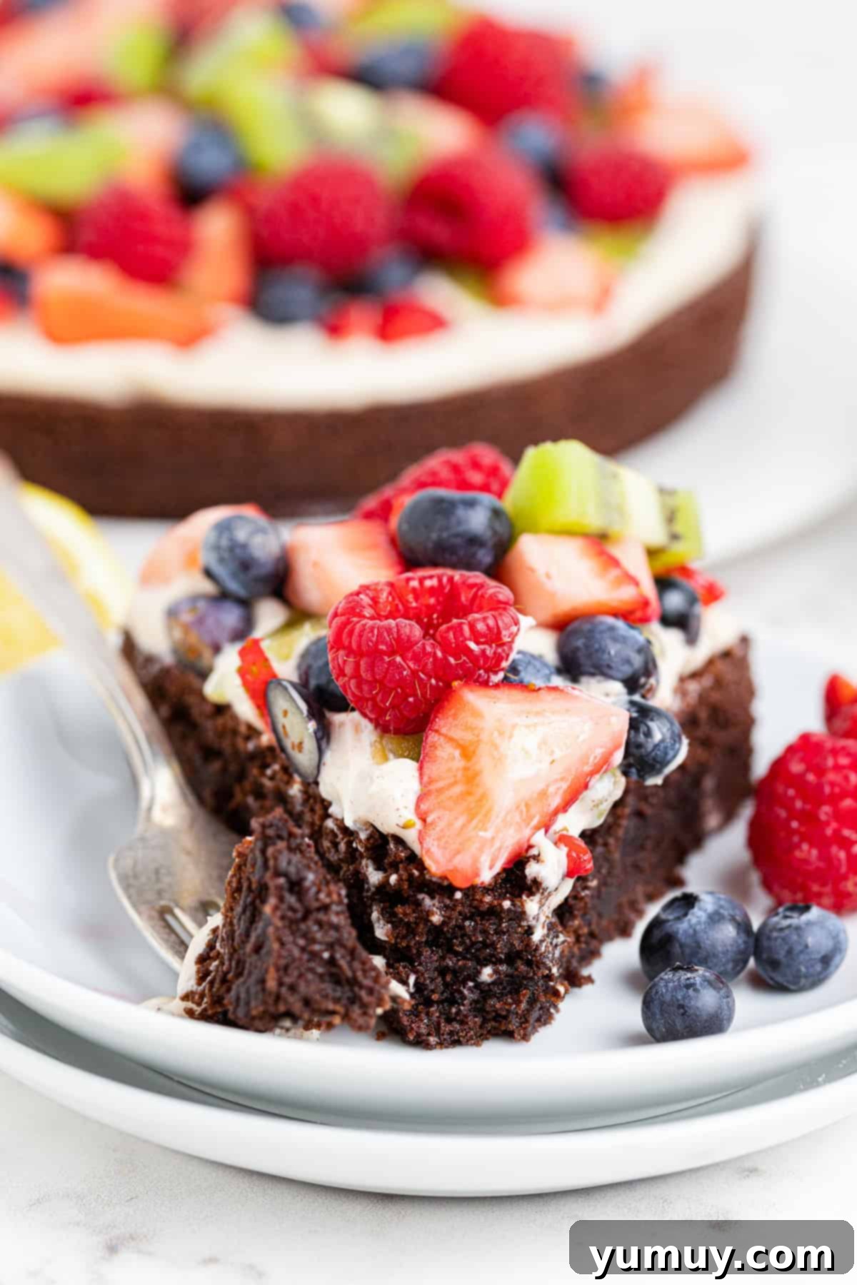 A slice taken out of a vibrant brownie fruit pizza, revealing its creamy topping and fresh fruit.