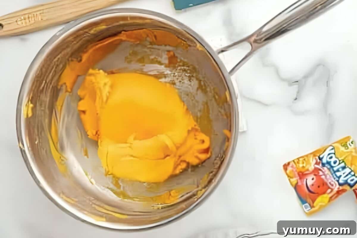 Fun Fragrant Kool Aid Playdough 13 Vibrant orange dough forming and thickening in a saucepan over gentle heat, beginning to gather around the stirring spoon.