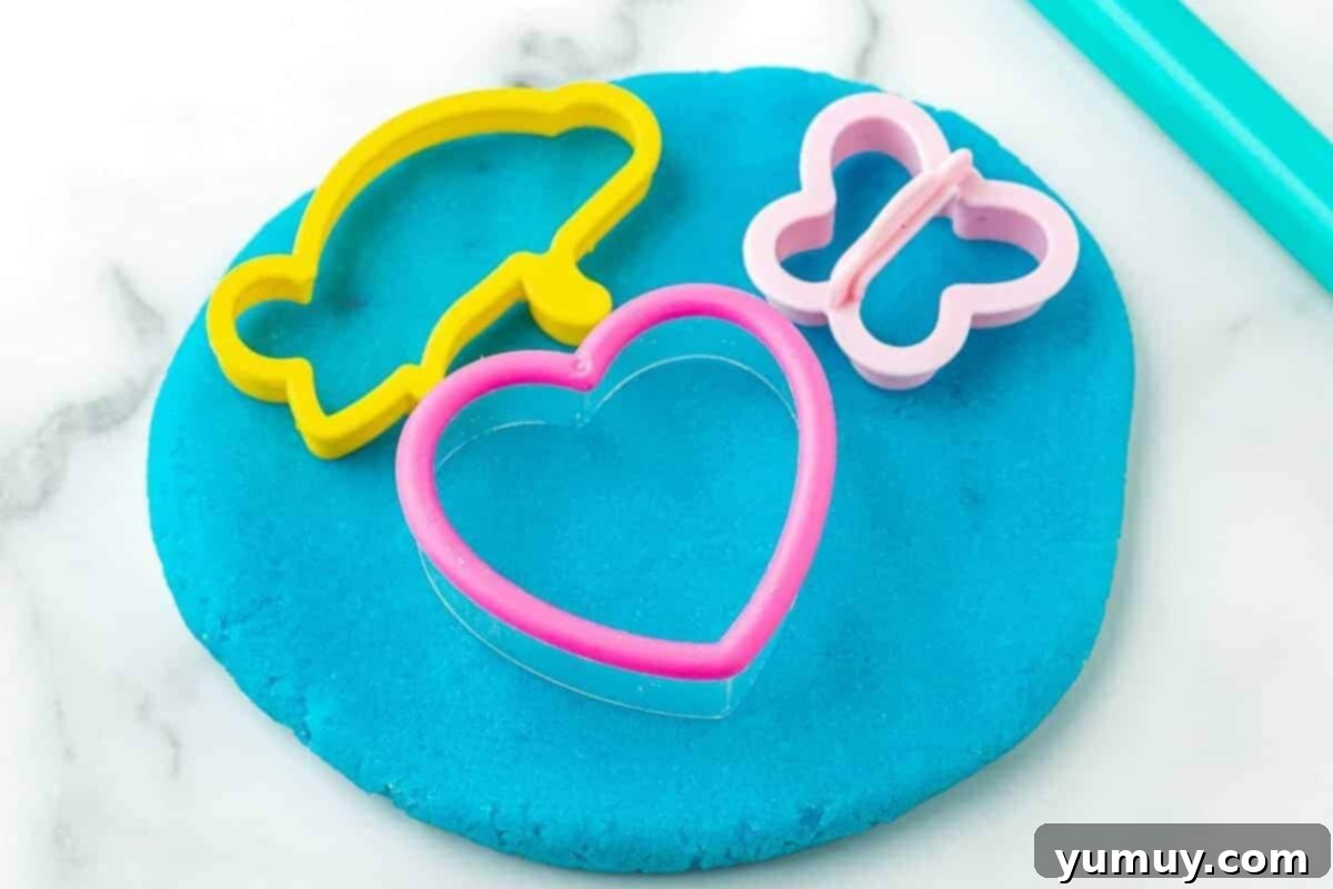 Fun Fragrant Kool Aid Playdough 3 A child's hands sculpting vibrant orange homemade playdough with various cookie cutters, showcasing the engaging and creative possibilities.