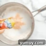 Fun Fragrant Kool Aid Playdough 5 Adding Kool-Aid powder to a saucepan with flour and other dry ingredients.