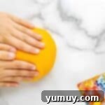 Fun Fragrant Kool Aid Playdough 8 Hands kneading vibrant orange homemade playdough on parchment paper until smooth.