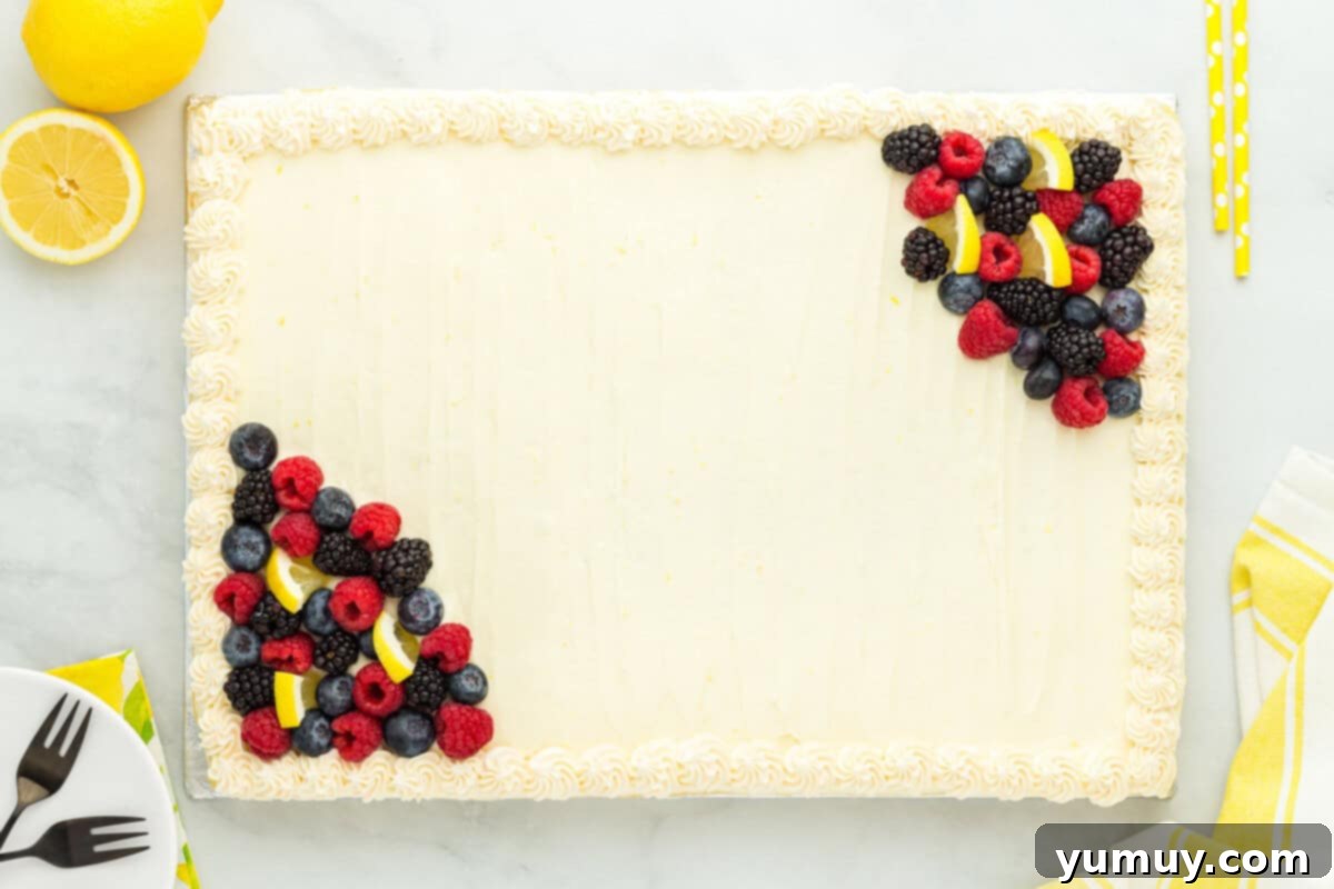 Sunshine Lemon Sheet Cake 14 A gloriously frosted lemon sheet cake adorned with fresh berries and lemon slices, beautifully presented on a wooden table, inviting a delicious slice.