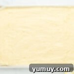 Sunshine Lemon Sheet Cake 6 smoothly spread lemon cake batter in a rectangular baking pan, ready for the oven.