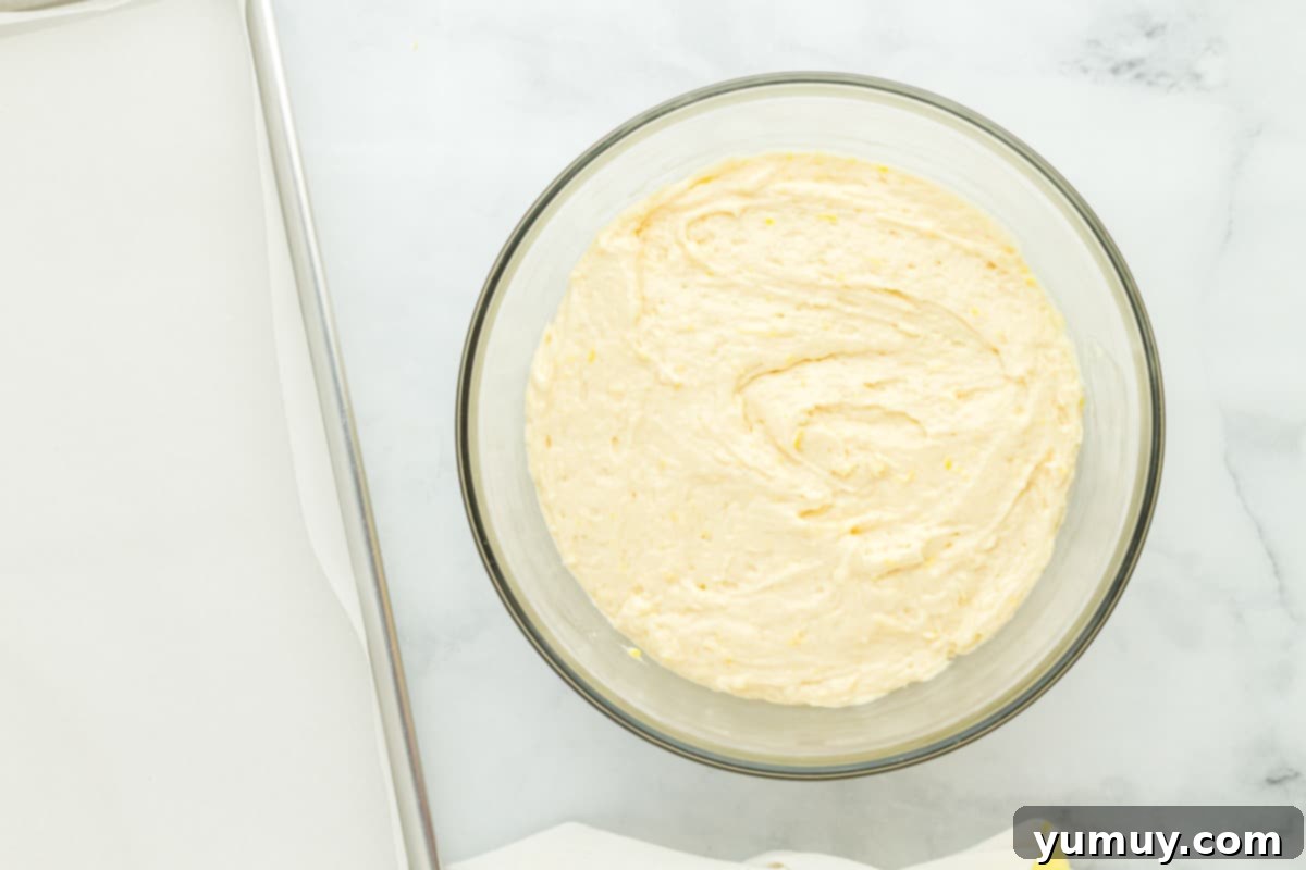 Sunshine Lemon Sheet Cake 10 Smooth lemon cake batter in a clear glass bowl, resting on a sophisticated marble countertop, ready for baking.