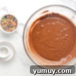 a bowl of chocolate ganache with sprinkles and a whisk.