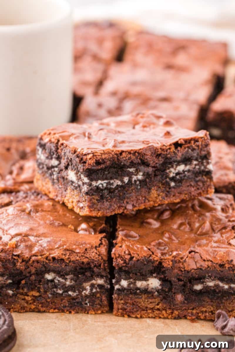 A close-up shot of a platter of freshly baked Slutty Brownies, showing the distinct layers of cookie, Oreo, and brownie, with one brownie having a bite taken out, revealing its rich interior.