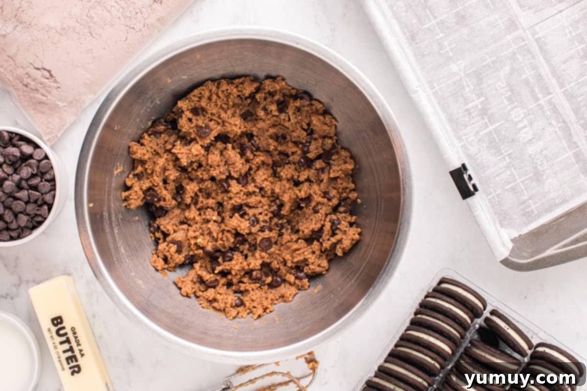 Chocolate chip cookie dough being mixed in a bowl with wet ingredients, forming a cohesive dough.