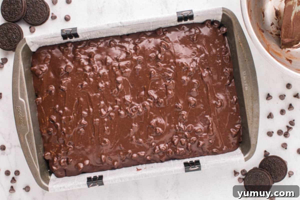 Brownie batter poured evenly over the Oreo layer in the baking pan, ready for the oven.