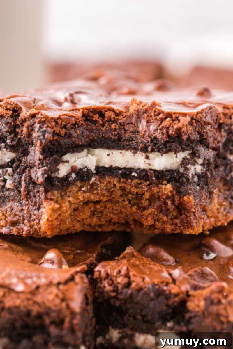 A close-up of a single Slutty Brownie with a corner bitten off, showcasing the distinct layers of cookie, Oreo, and fudgy brownie.