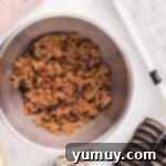 Chocolate chip cookie dough being mixed in a bowl with melted butter and an egg.