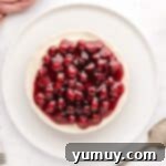 A whole no-bake cherry cheesecake on a serving plate, generously topped with glistening cherry pie filling.