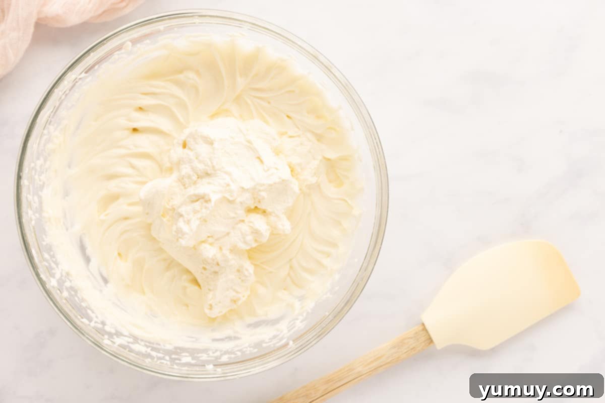 A bowl of perfectly whipped heavy cream with stiff peaks, ready to be folded into the cheesecake mixture.