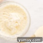 Freshly whipped heavy cream in a clear glass bowl, showing stiff peaks, next to a wooden spoon.