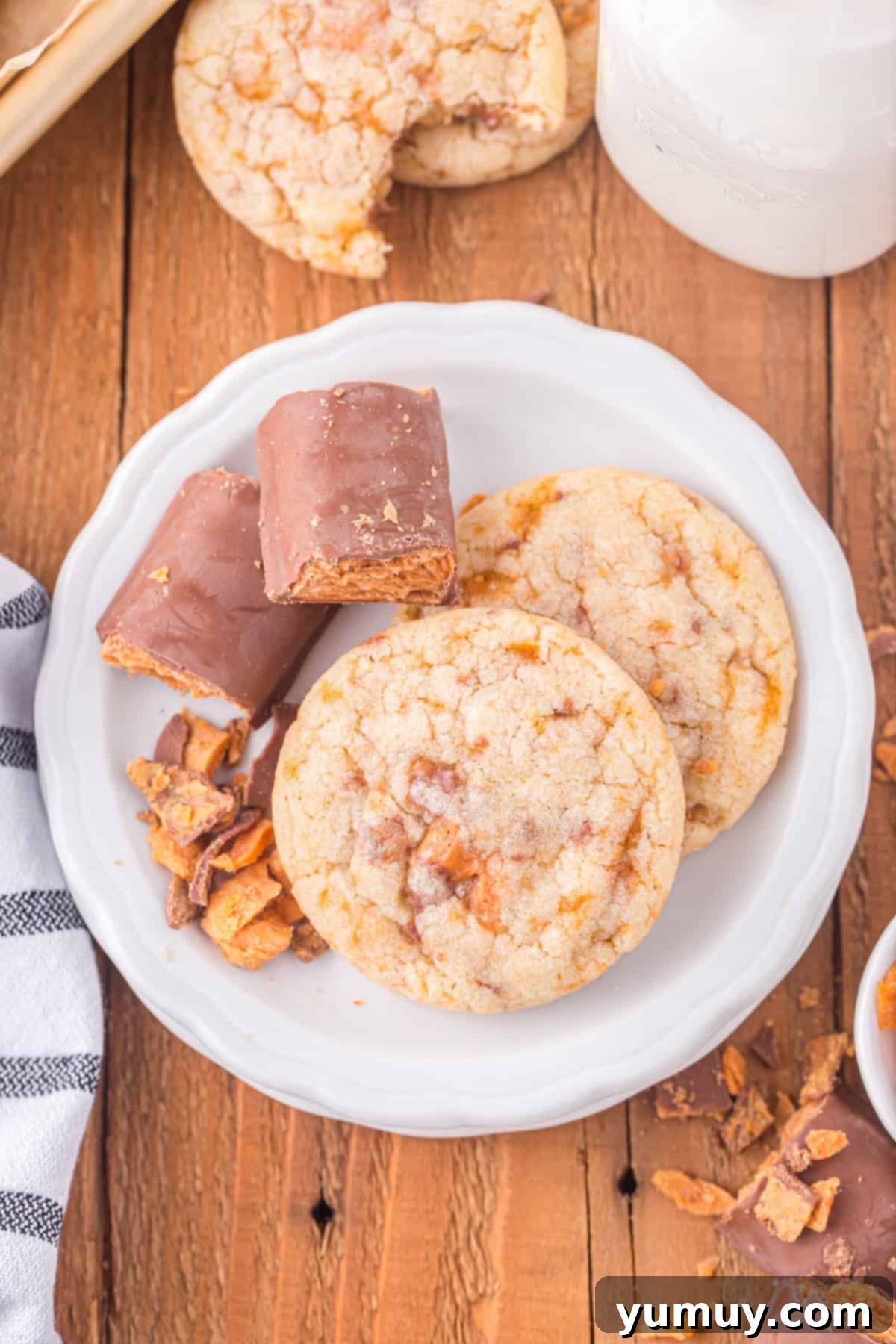 A plate of golden-brown Butterfinger cookies and a refreshing glass of milk, inviting you to indulge in this sweet treat.
