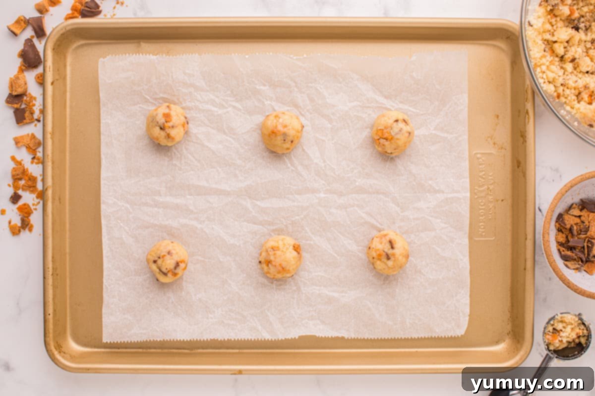 Rolled cookie dough balls with visible Butterfinger chunks, neatly arranged on a parchment-lined baking sheet, ready for the oven.
