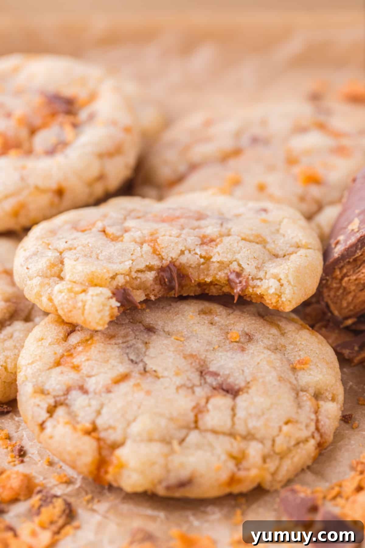 A close-up shot of a group of homemade Butterfinger cookies, with one cookie showing a bite taken out, revealing the soft interior and crunchy candy pieces.