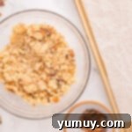 A bowl of cookie dough with Butterfinger pieces folded in, next to a cookie scoop.