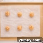 Cookie dough balls with Butterfinger chunks arranged on a parchment-lined baking sheet, spaced for even baking.