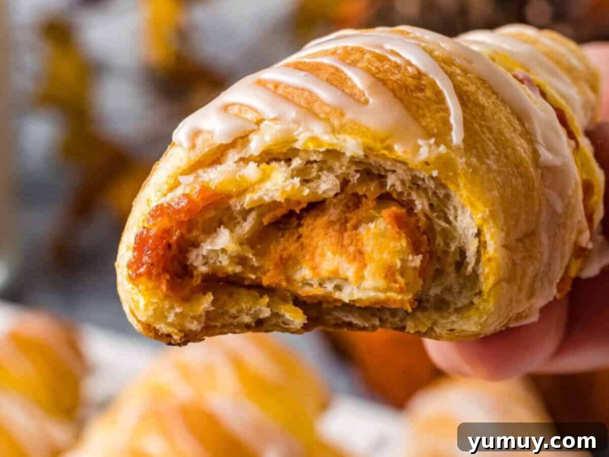 Effortless Pumpkin Puree Delights 5 close up on a pumpkin pie stuffed crescent roll with a bite taken out to reveal the interior.