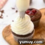 piping stabilized whipped cream frosting on black forest cupcakes with a piping tip.