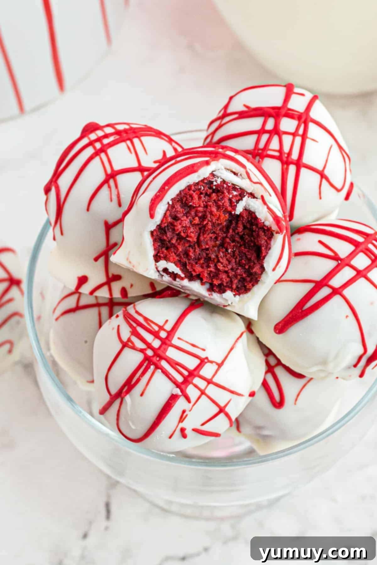 A bitten red velvet cake truffle in a glass bowl with more truffles, showcasing its moist interior and white chocolate coating.