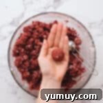 Hands rolling red velvet cake and frosting mixture into perfectly round cake balls, ready for chilling.