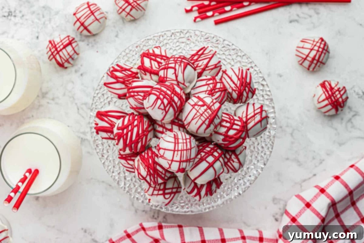 Overhead view of decorated red velvet cake truffles piled elegantly on a glass cake stand, featuring both white chocolate coating and festive red drizzles.