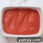 Red velvet cake batter spread evenly into a 9x13-inch greased baking pan, perfectly smooth and ready for the oven.