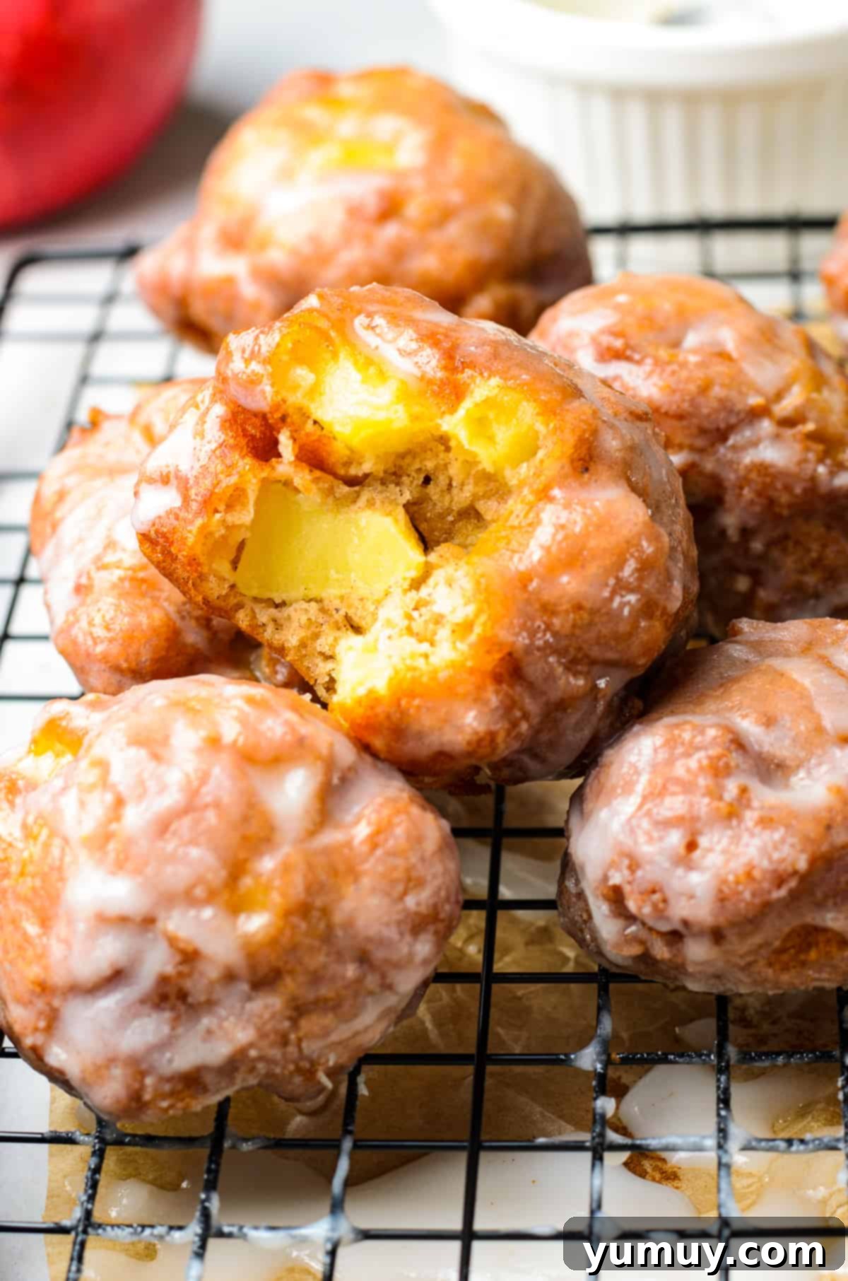 A stack of golden glazed apple fritters, with a bite taken out of one, showcasing the tender apple pieces inside.
