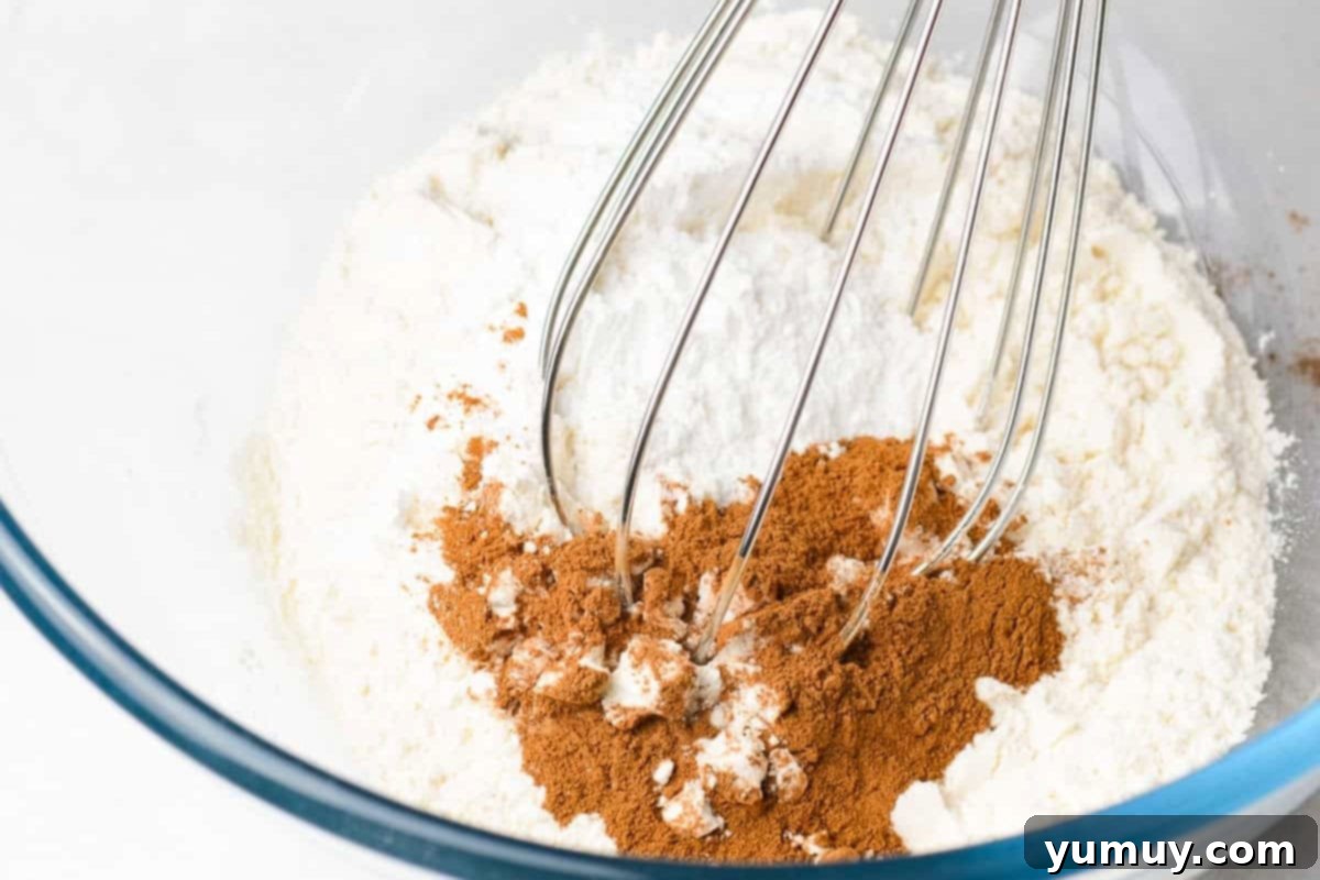 All-purpose flour and ground cinnamon in a clear glass bowl, being whisked together.