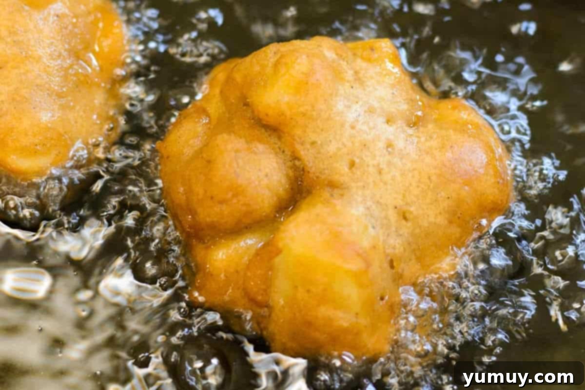 Several apple fritters frying in hot vegetable oil in a Dutch oven, turning golden brown.