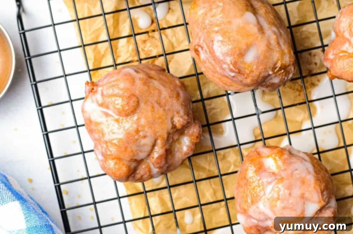 Freshly deep fried apple fritters resting on a cooling rack, glistening with glaze.