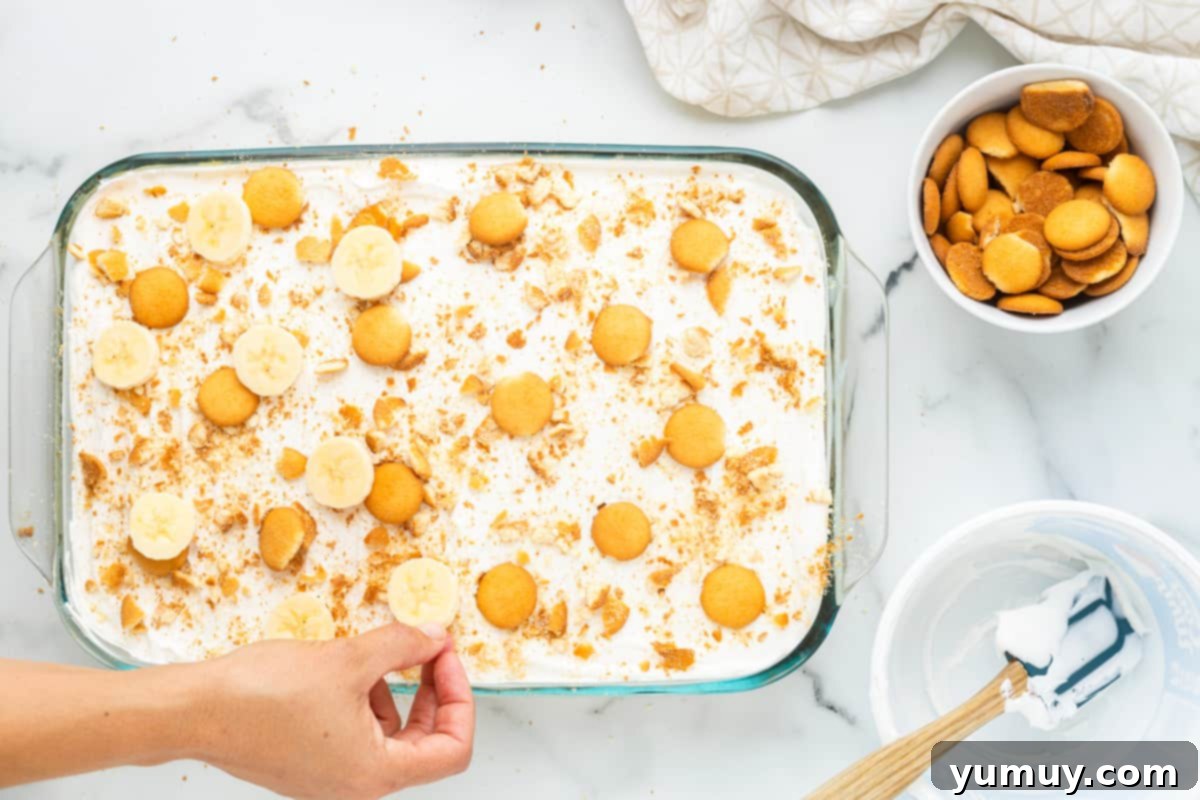 hand placing sliced bananas on top of banana cream pie poke cake