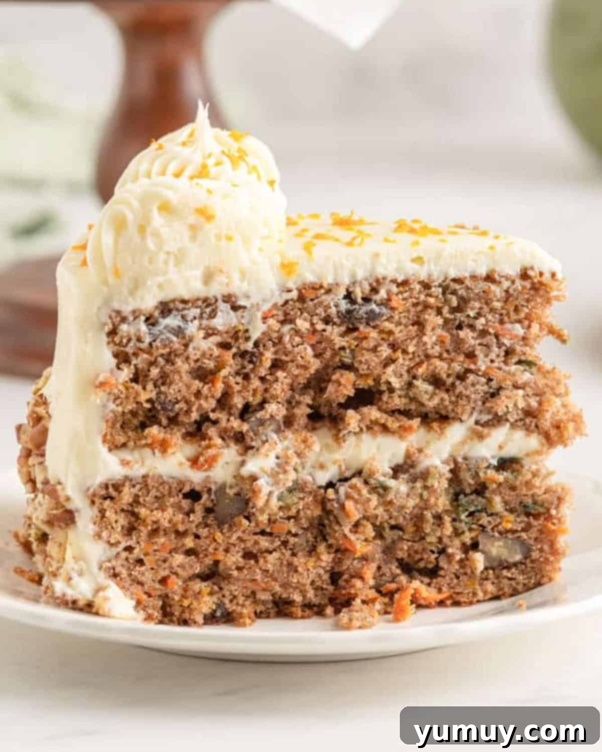 side view of a slice of orange carrot cake on a white plate, showcasing moist layers and creamy frosting.