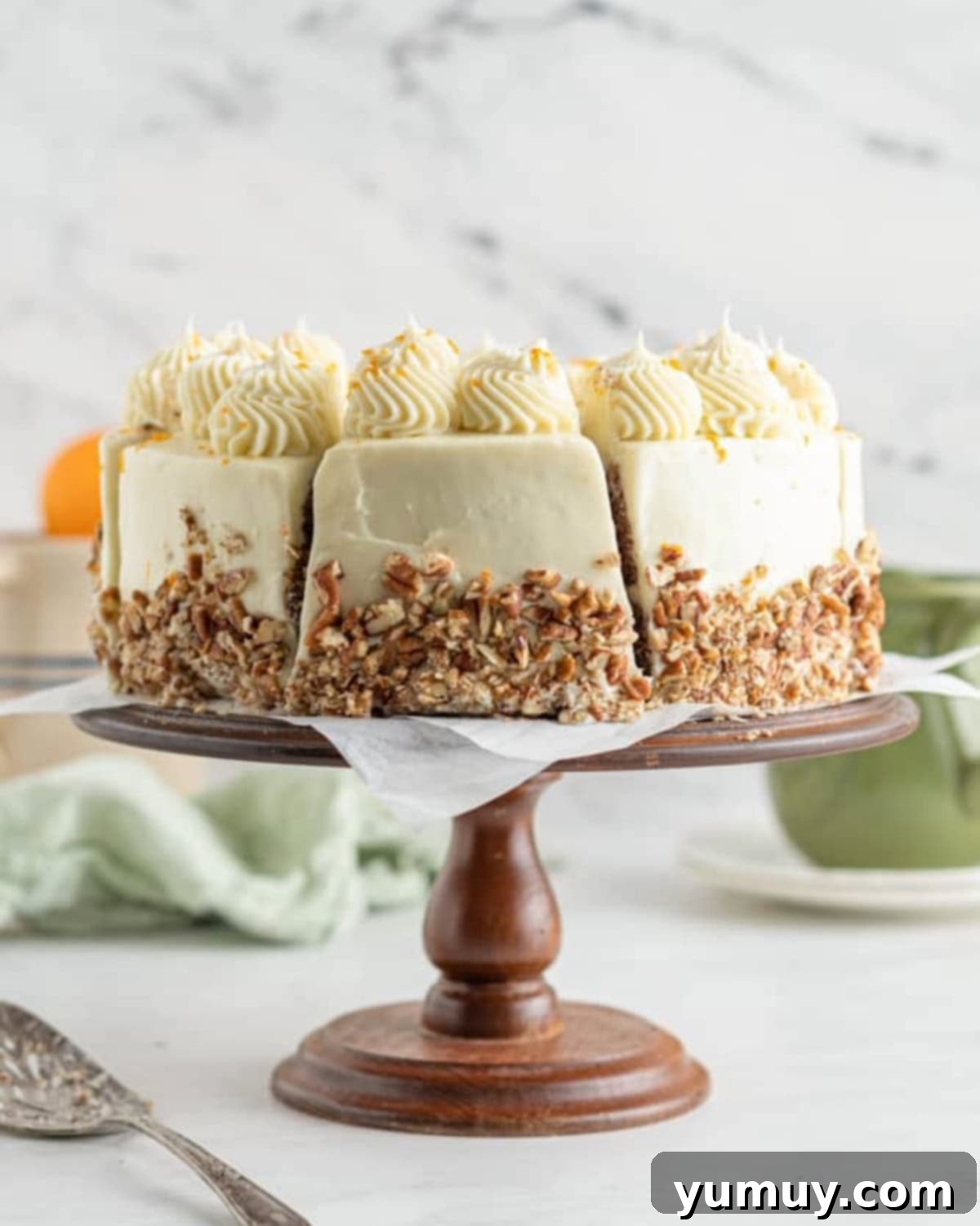 side view of a sliced orange carrot cake on a cake stand, revealing its layered structure.