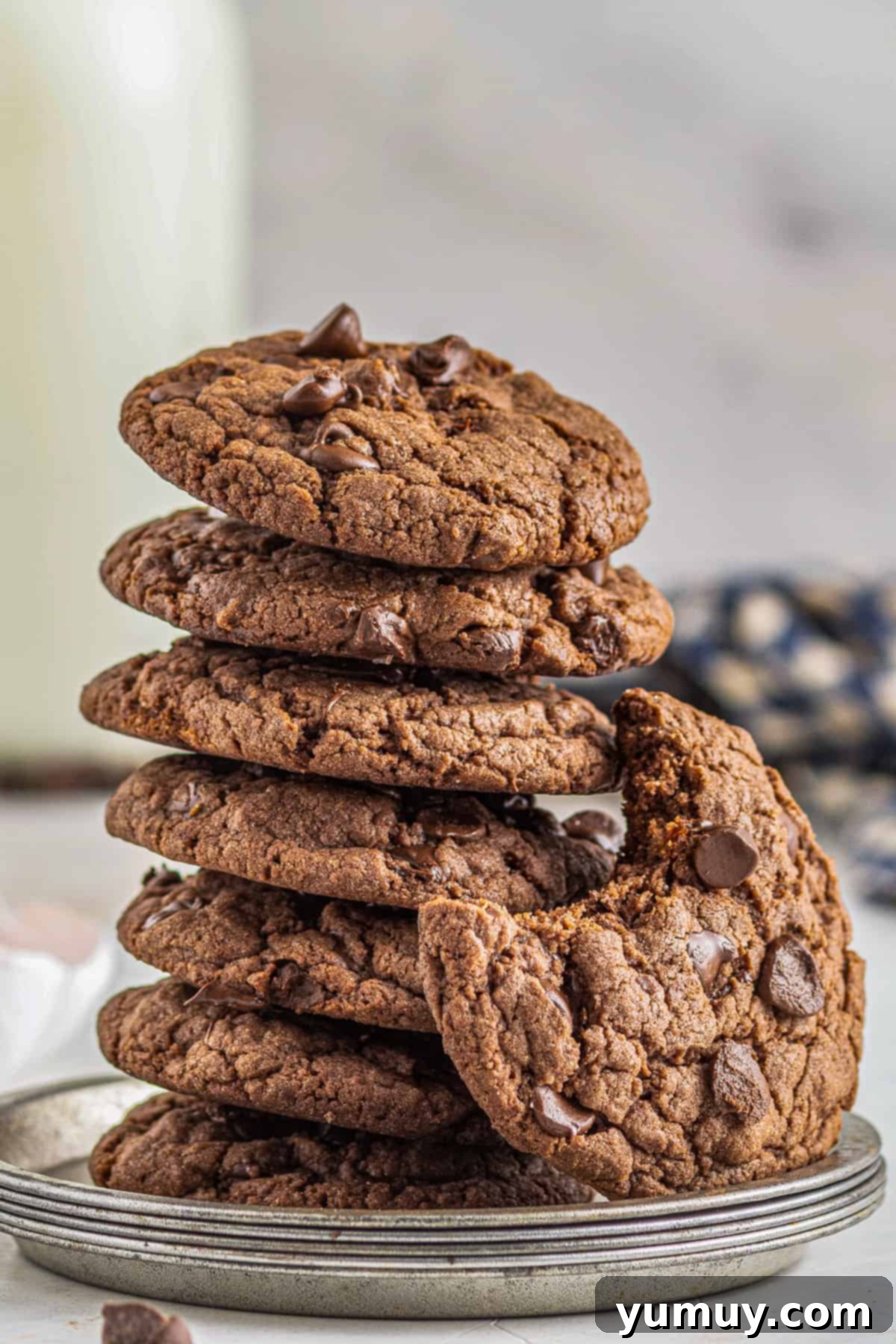 A perfectly stacked pile of chocolate cake mix cookies, showcasing their rich color and abundant chocolate chips, with one cookie bitten into on the side.