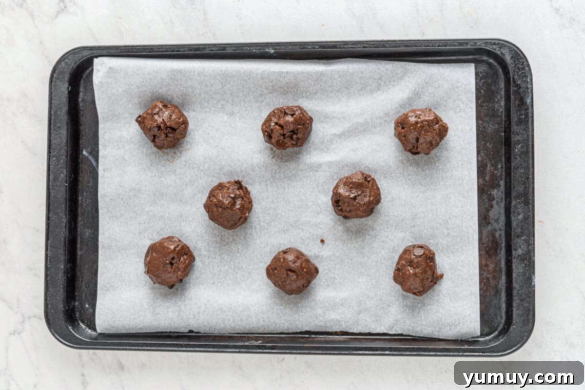 Eight perfectly portioned chocolate cake mix cookies, brimming with chocolate chips, arranged on a parchment-lined baking sheet, ready for the oven.