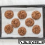 8 chocolate cookies with chocolate chips on a parchment lined baking sheet after baking