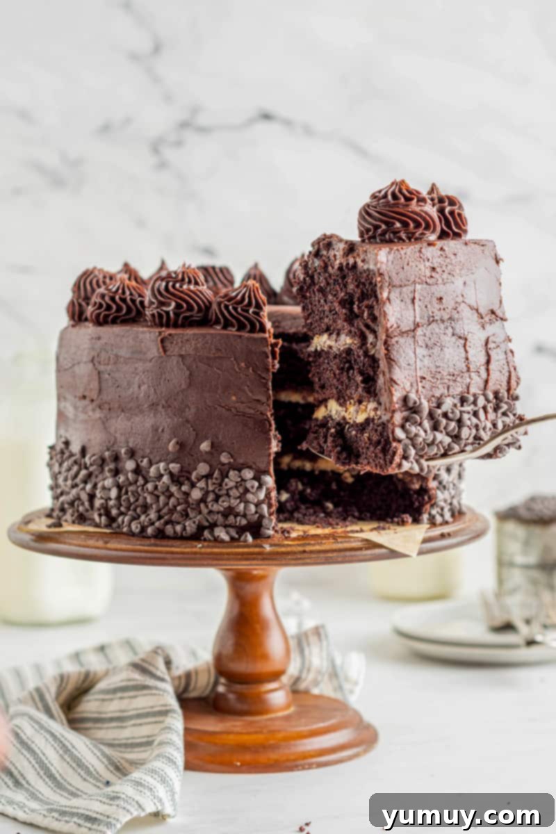 A glorious slice of chocolate cookie dough layer cake being lifted from the full cake, revealing its decadent layers of chocolate cake and cookie dough filling, perched on a pristine white cake server.