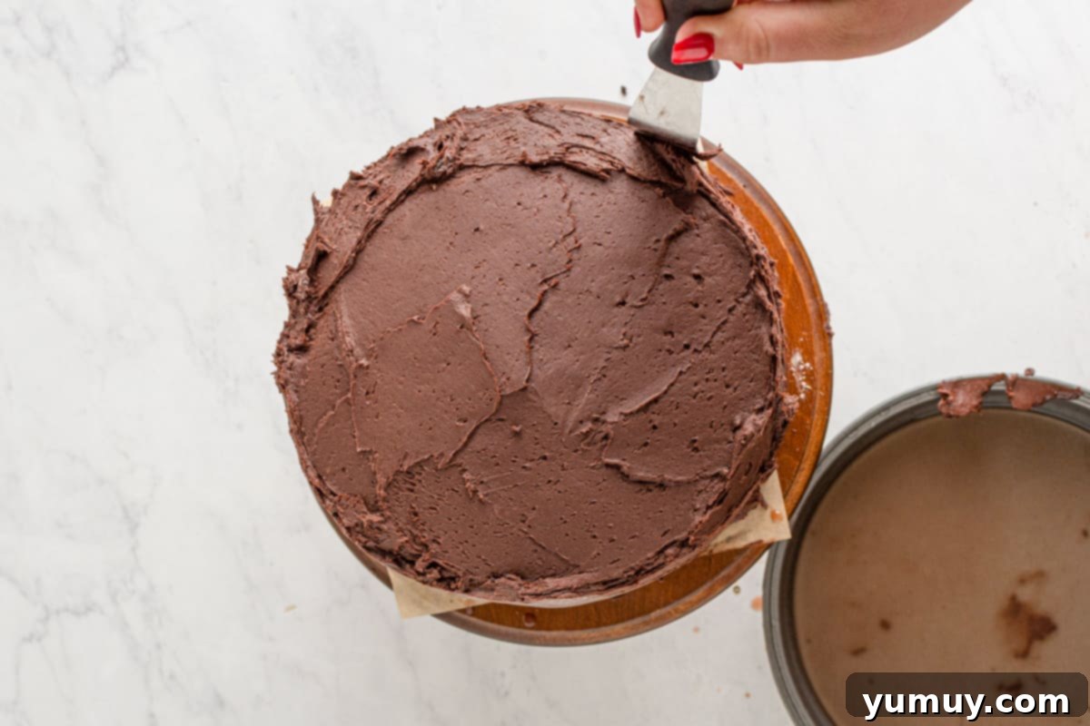 A skilled hand demonstrates the technique of spreading chocolate frosting onto a cake with an offset spatula, creating a beautifully smooth and even layer.