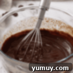 Decadent Chocolate Dream Cake 11 chocolate ganache in a glass bowl with a whisk.